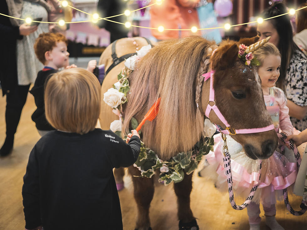 3 children grooming pony with unicorn horn. 